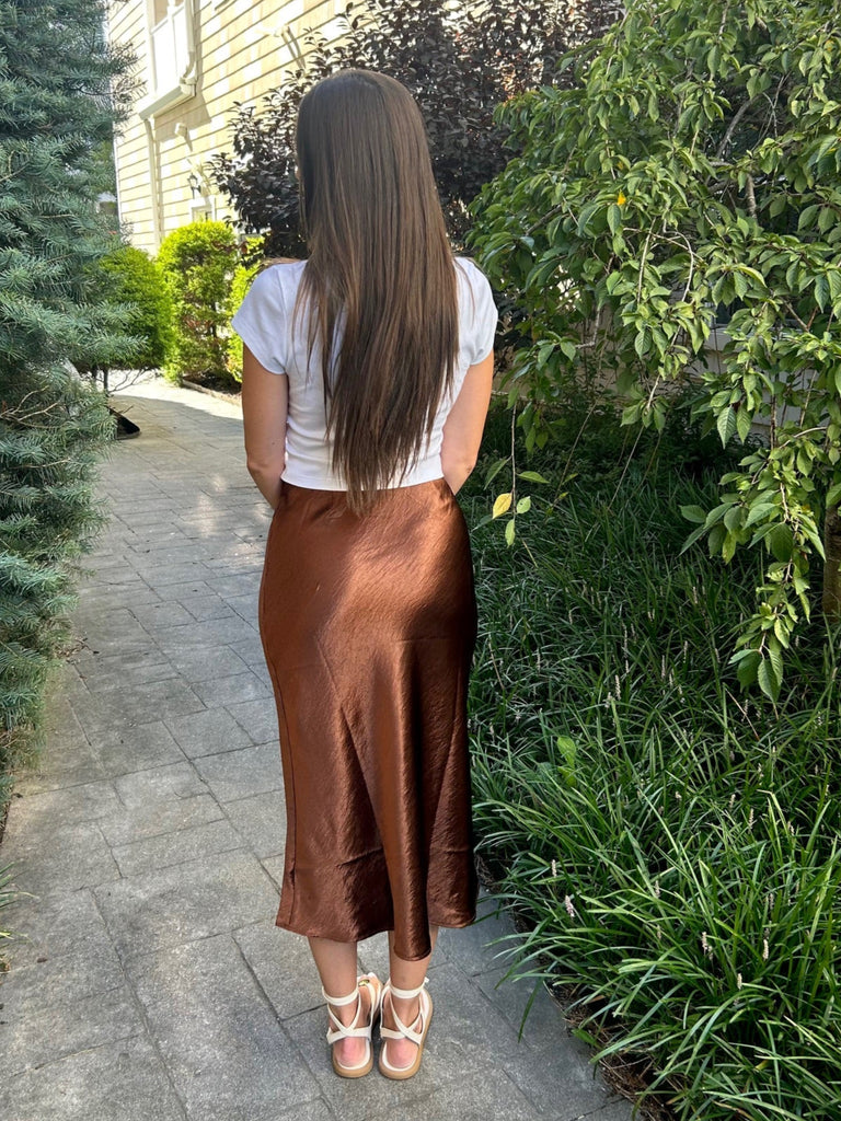 Woman walking on a sidewalk with greenery and a building in the background
