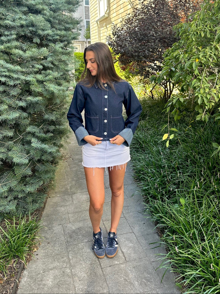 Woman standing on a sidewalk with greenery and a building in the background